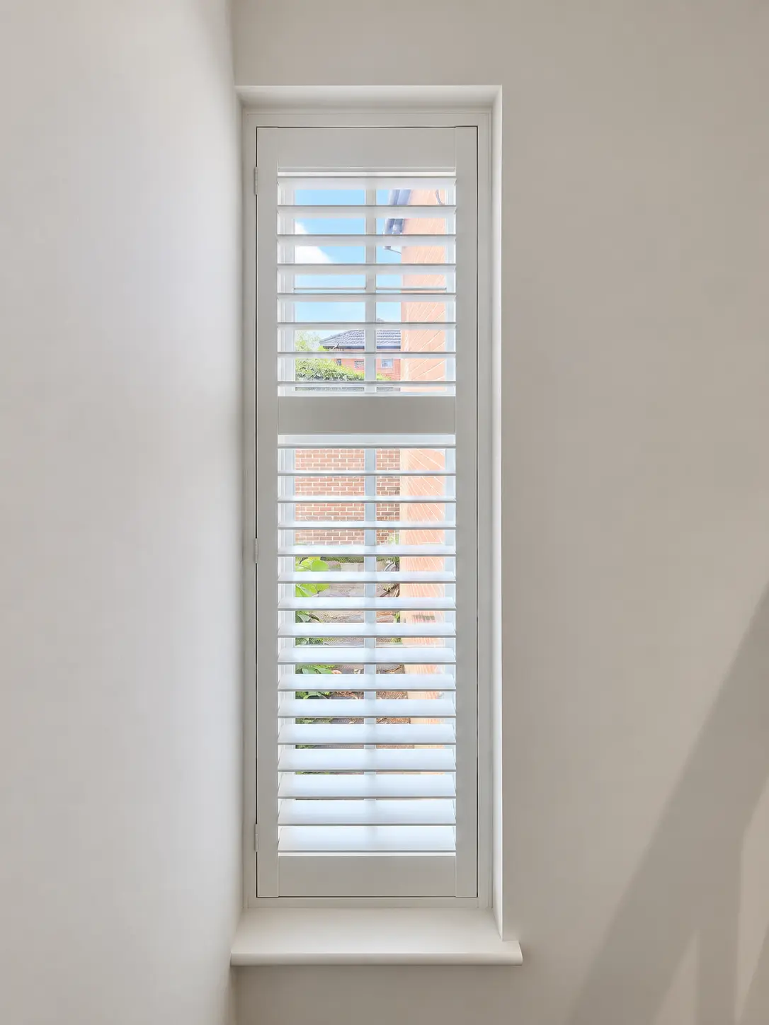 Full-height shutters at a tall, narrow hallway window in the Esher display house.