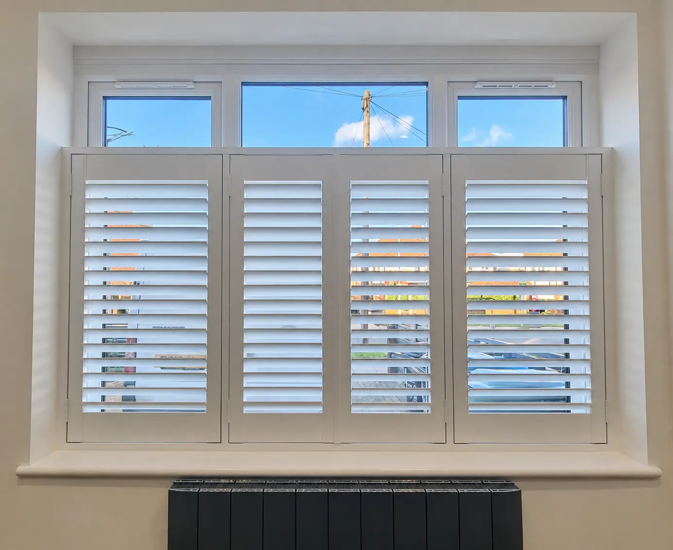 Four white cafe-style shutter panels covering the lower part of a living-room window, leaving the top panes uncovered.