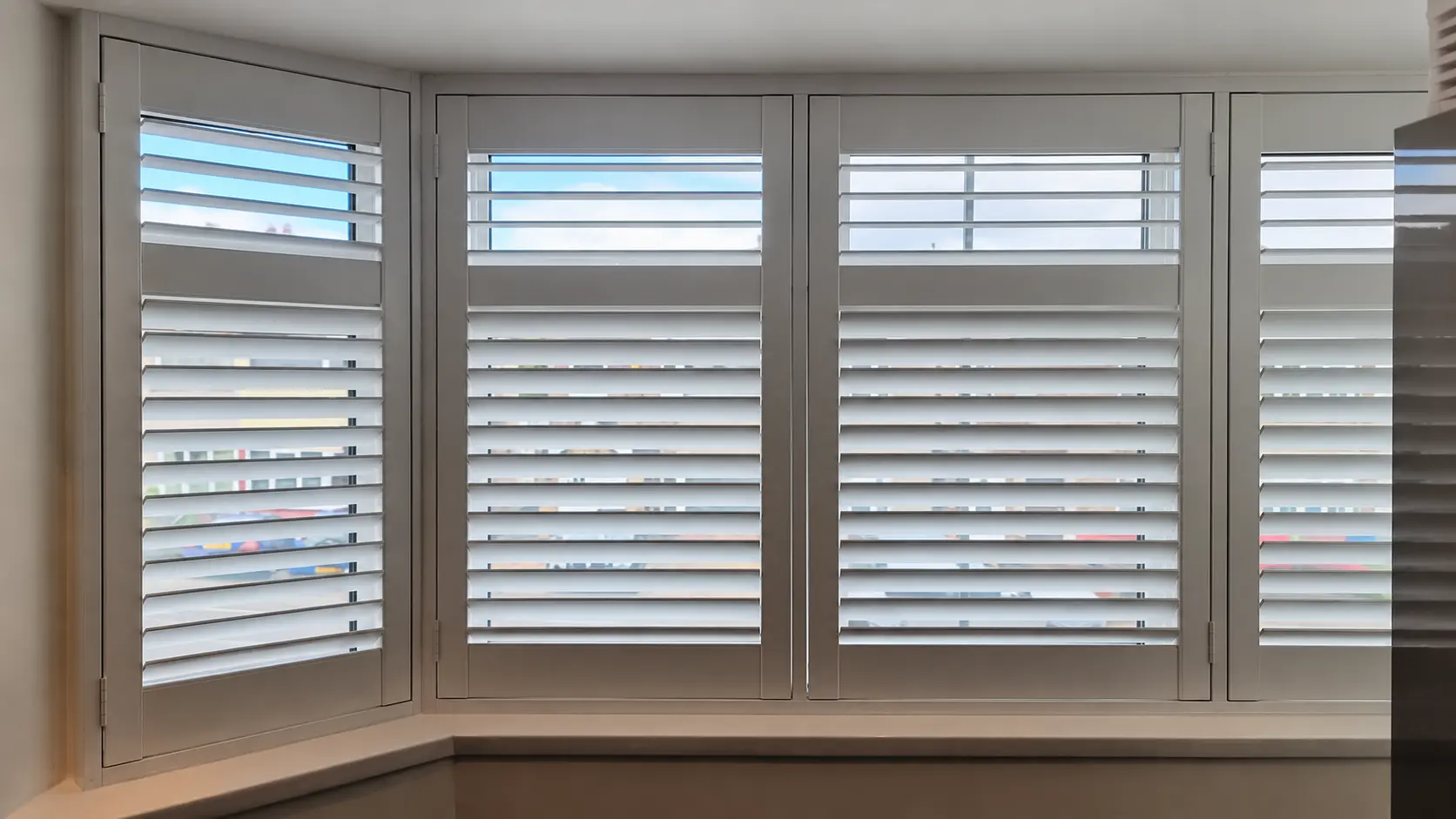 White full-height shutters following a bedroom bay window, with the upper louvres open wider than the lower louvres.