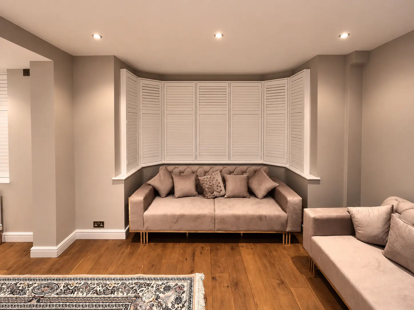 White full-height shutters with closed louvres in a living-room bay window behind a sofa.