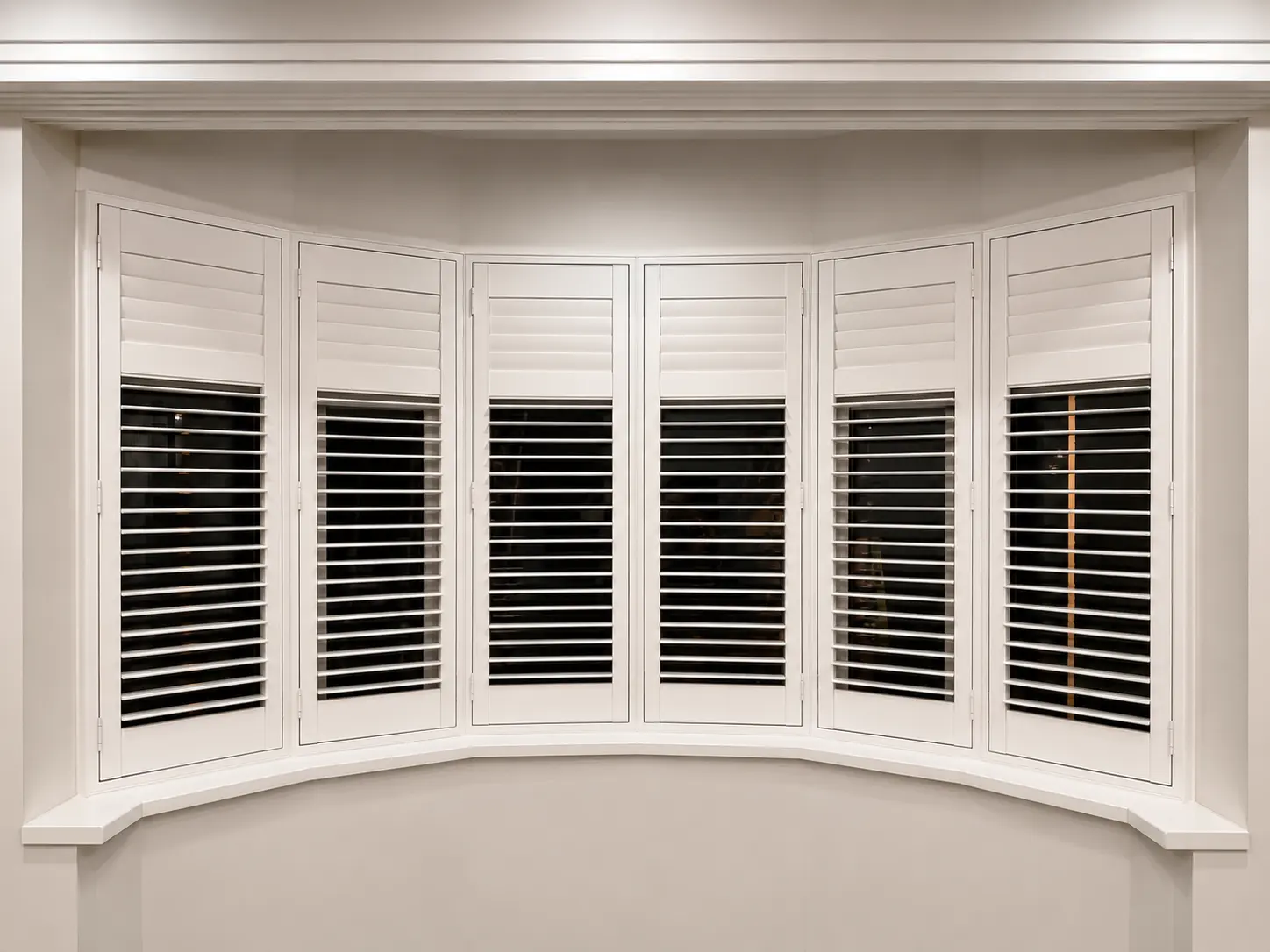 White full-height shutters following a curved living-room bay window, with upper louvres closed and lower louvres open against a dark exterior.