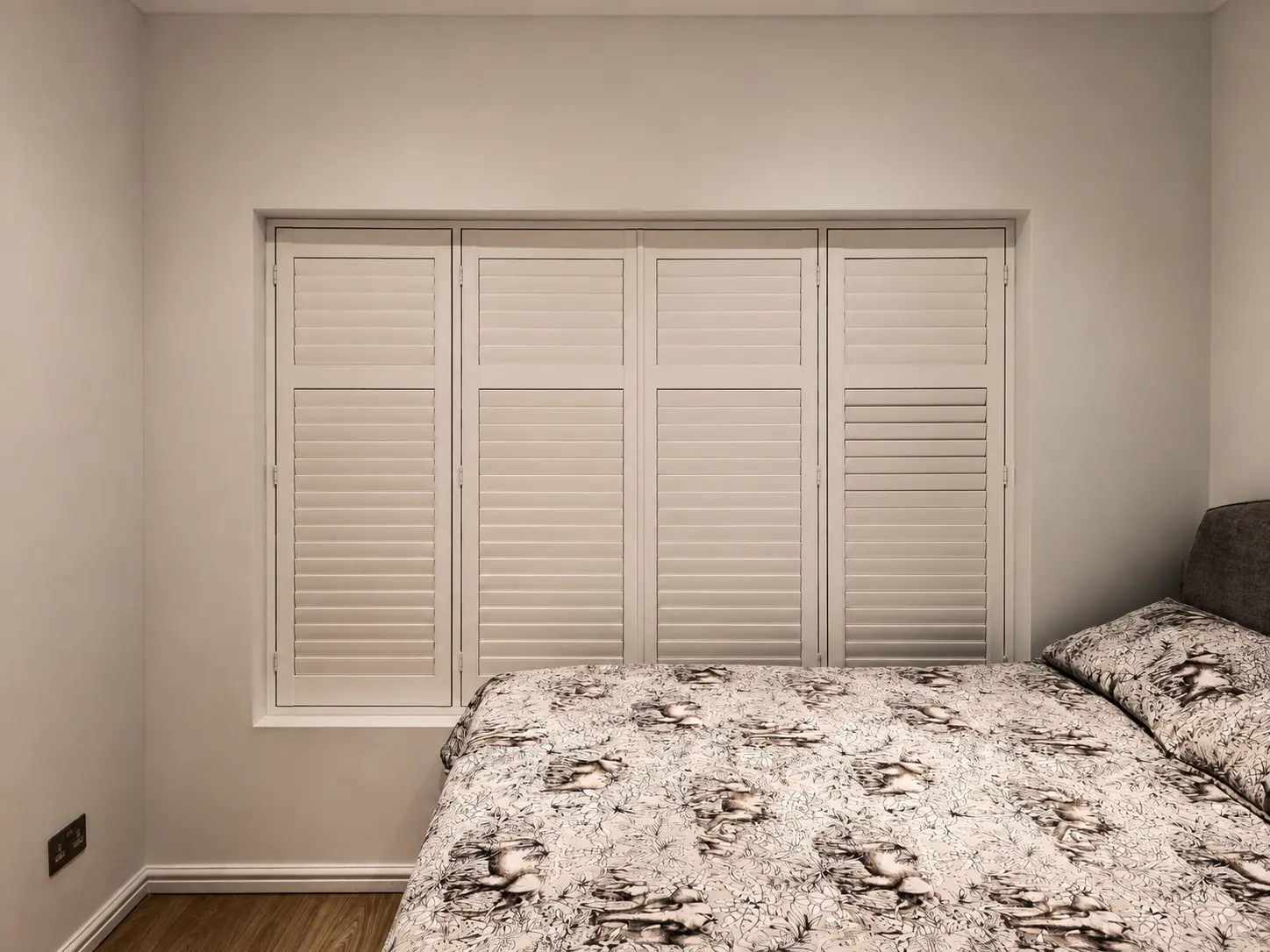 Four white full-height shutter panels with closed louvres beside a bed.