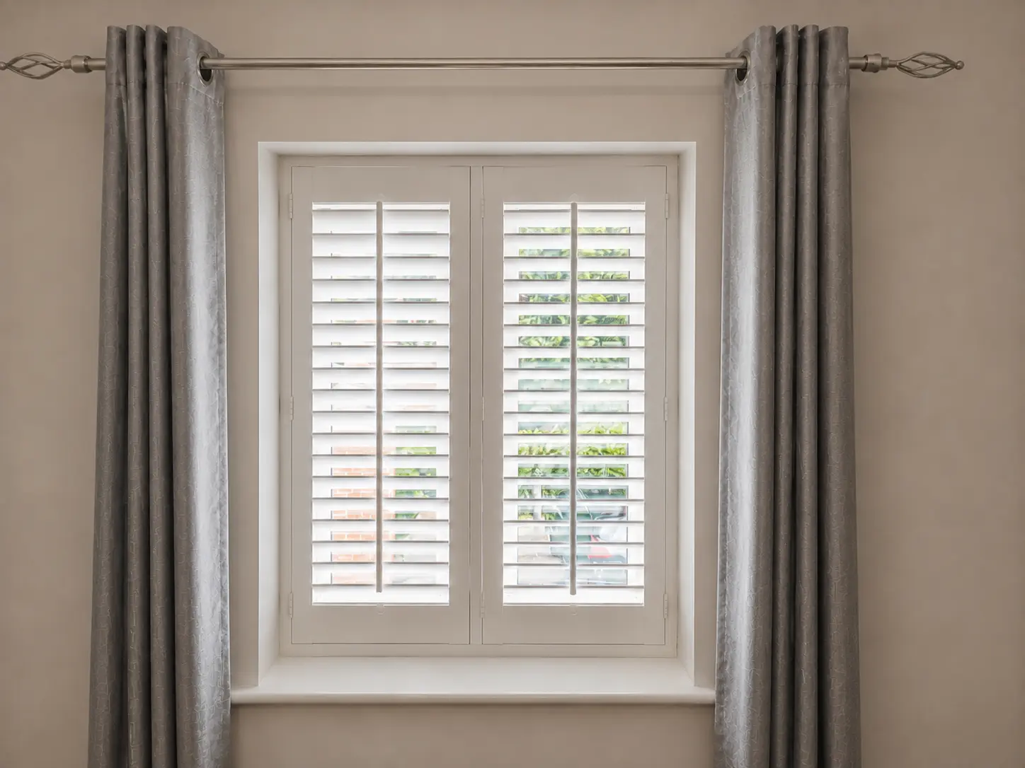 Two white full-height shutter panels at a bedroom window between grey curtains.