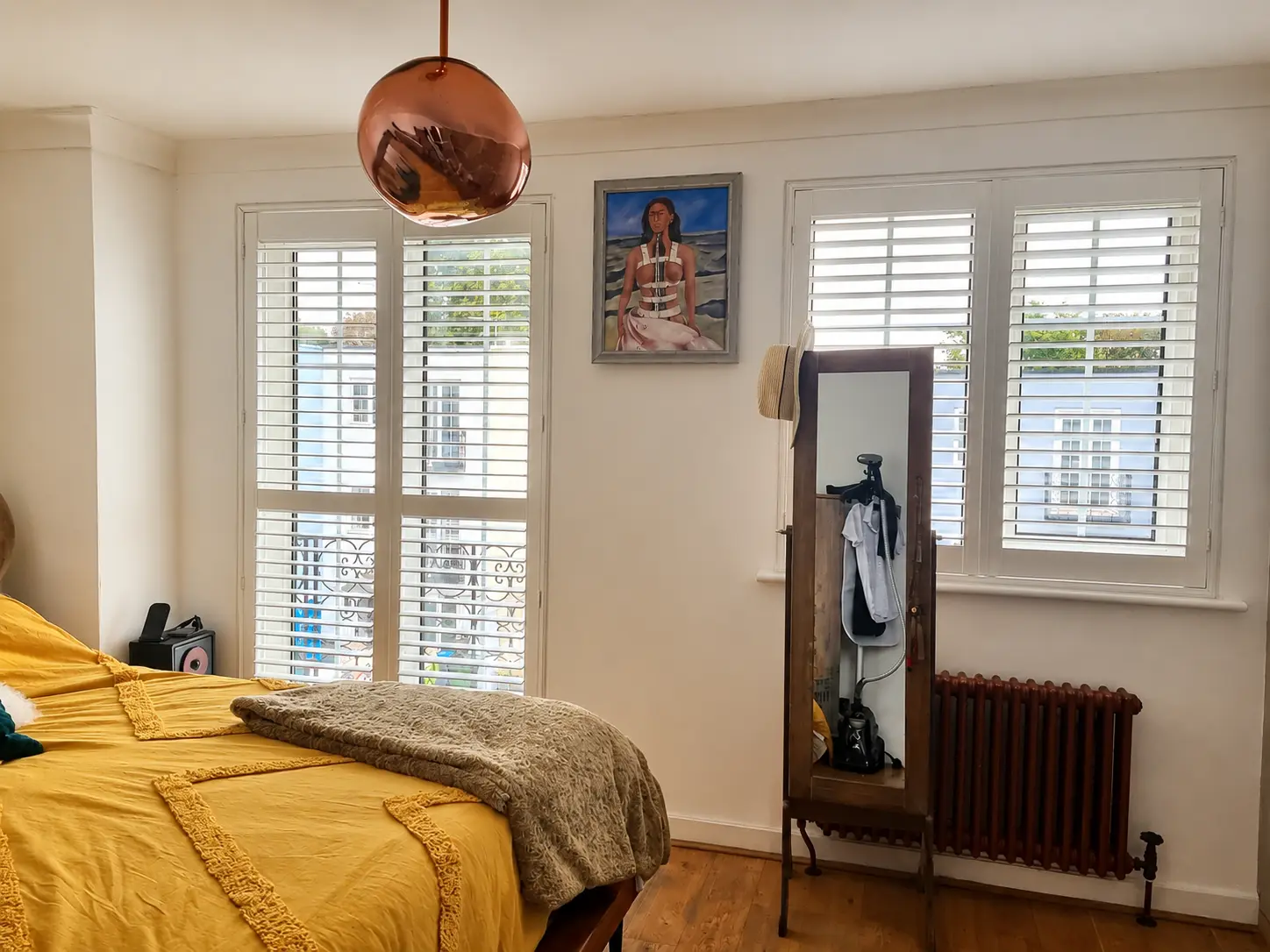 White full-height shutters covering a glazed bedroom door and a separate window beside a bed.