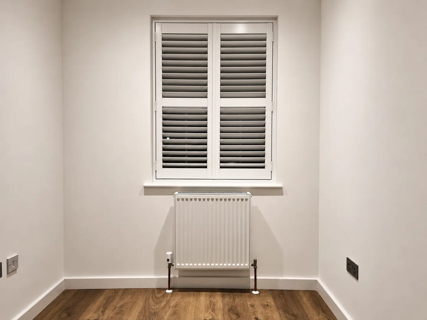 White full-height shutters with a central divider rail at a bedroom window above a radiator.