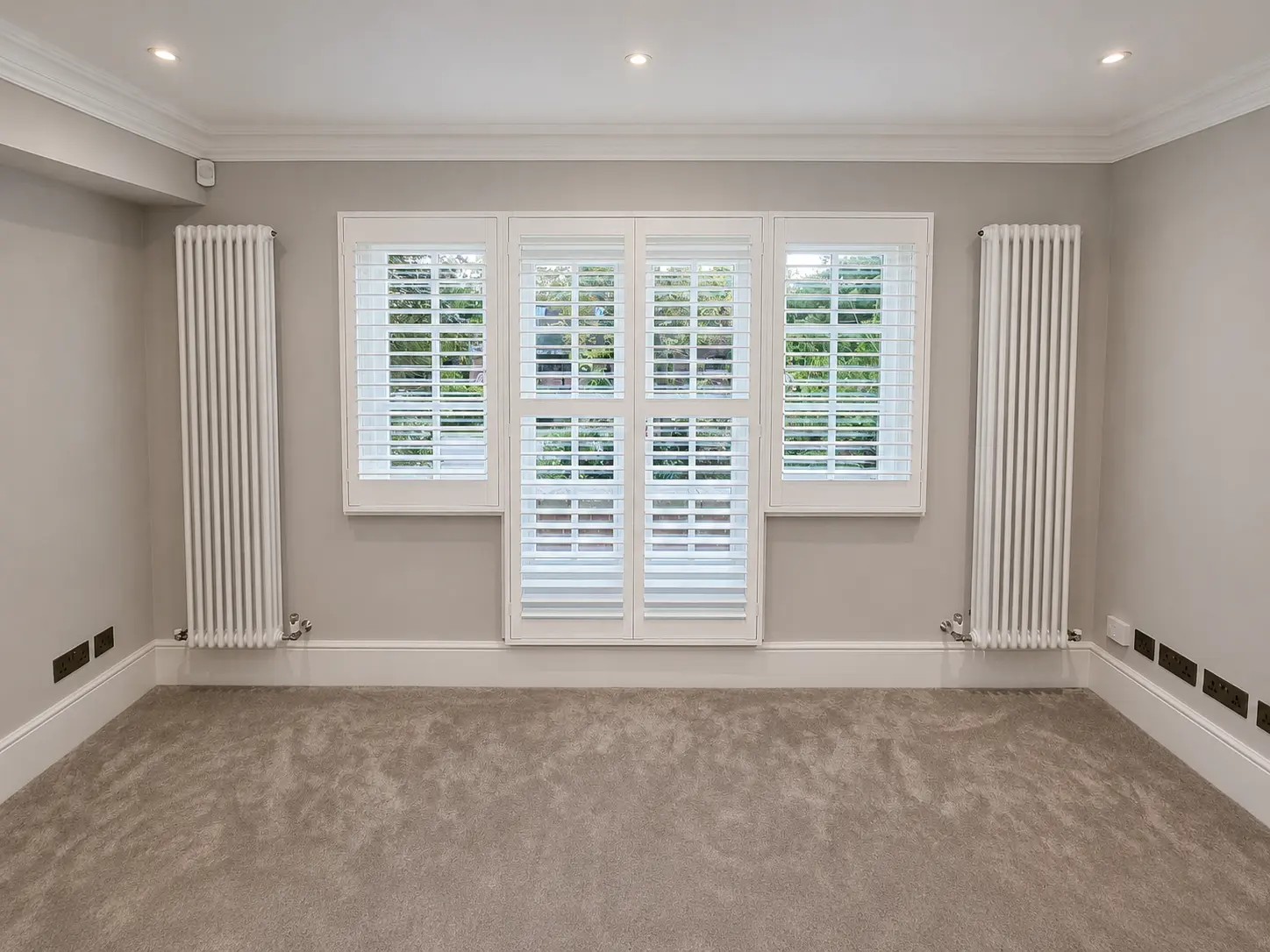 White full-height shutters covering bedroom windows and central glazed doors in an unfurnished room.