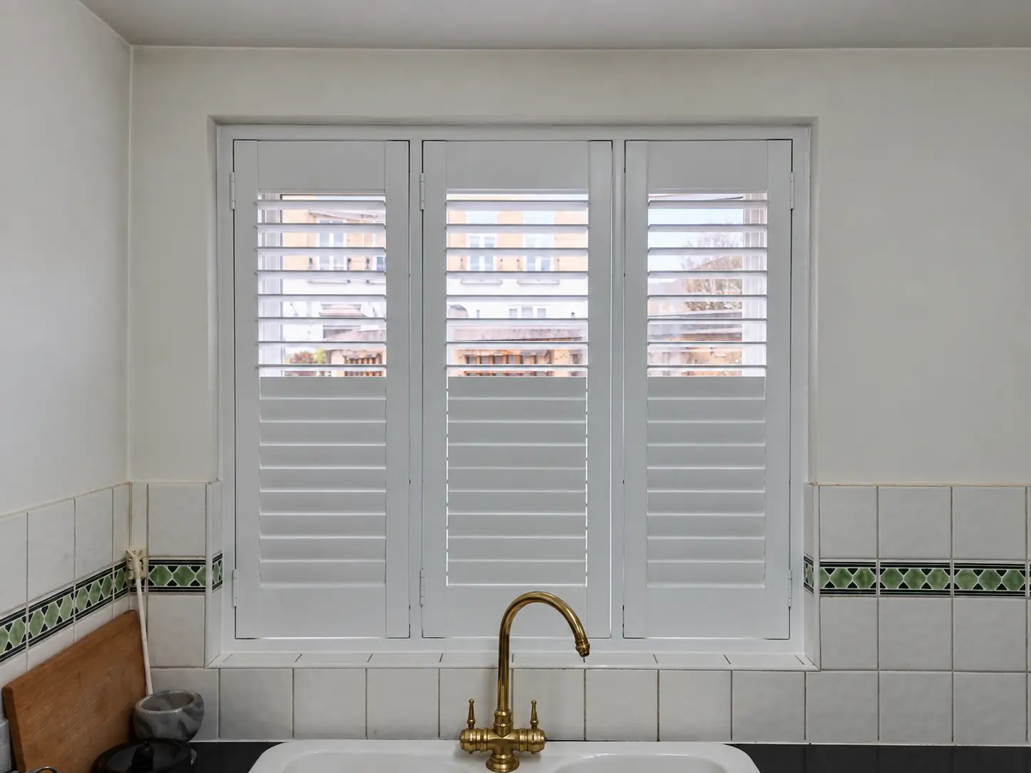 Three white full-height shutter panels above a kitchen sink, with upper louvres open and lower louvres closed.