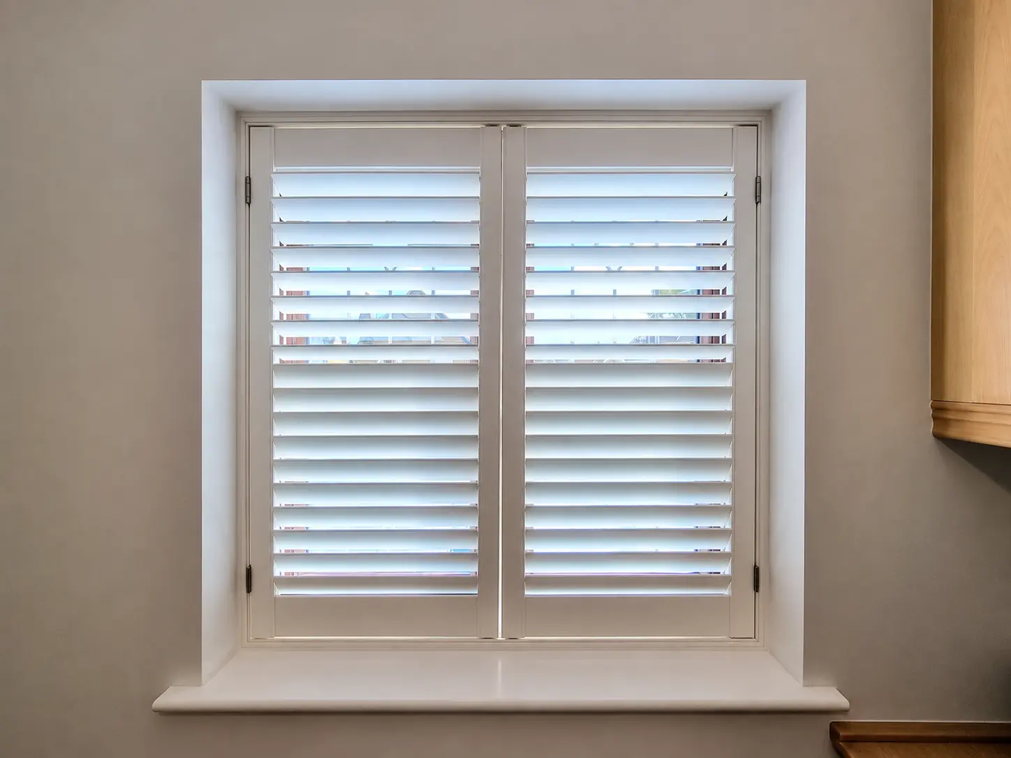 Two white full-height shutter panels at a kitchen window beside a wooden cabinet.