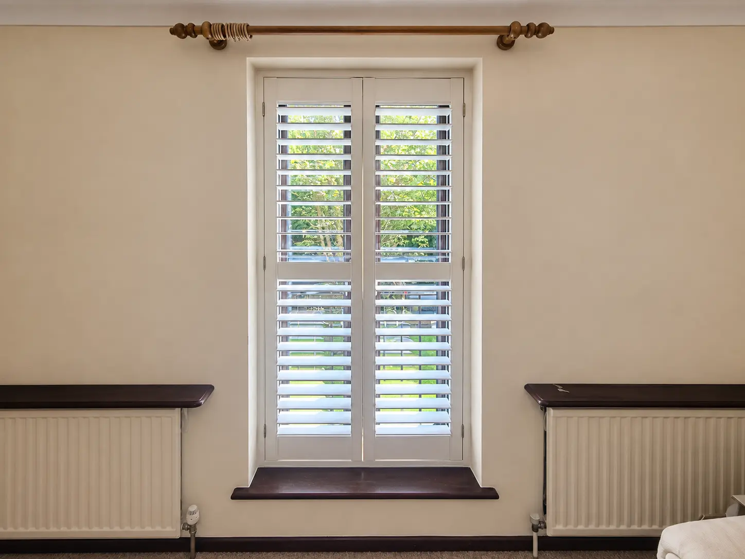 Two white full-height shutter panels with a divider rail at a tall living-room window between two radiators.