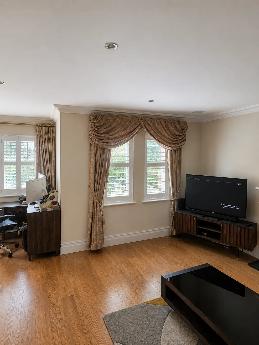 White full-height shutters at living-room windows with gold curtains above a wooden floor.