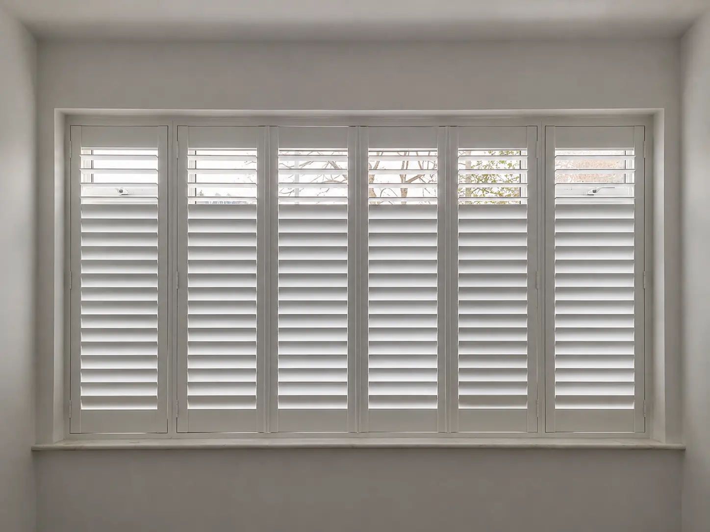 Six white full-height shutter panels across a wide living-room window, with upper louvres open and lower louvres closed.
