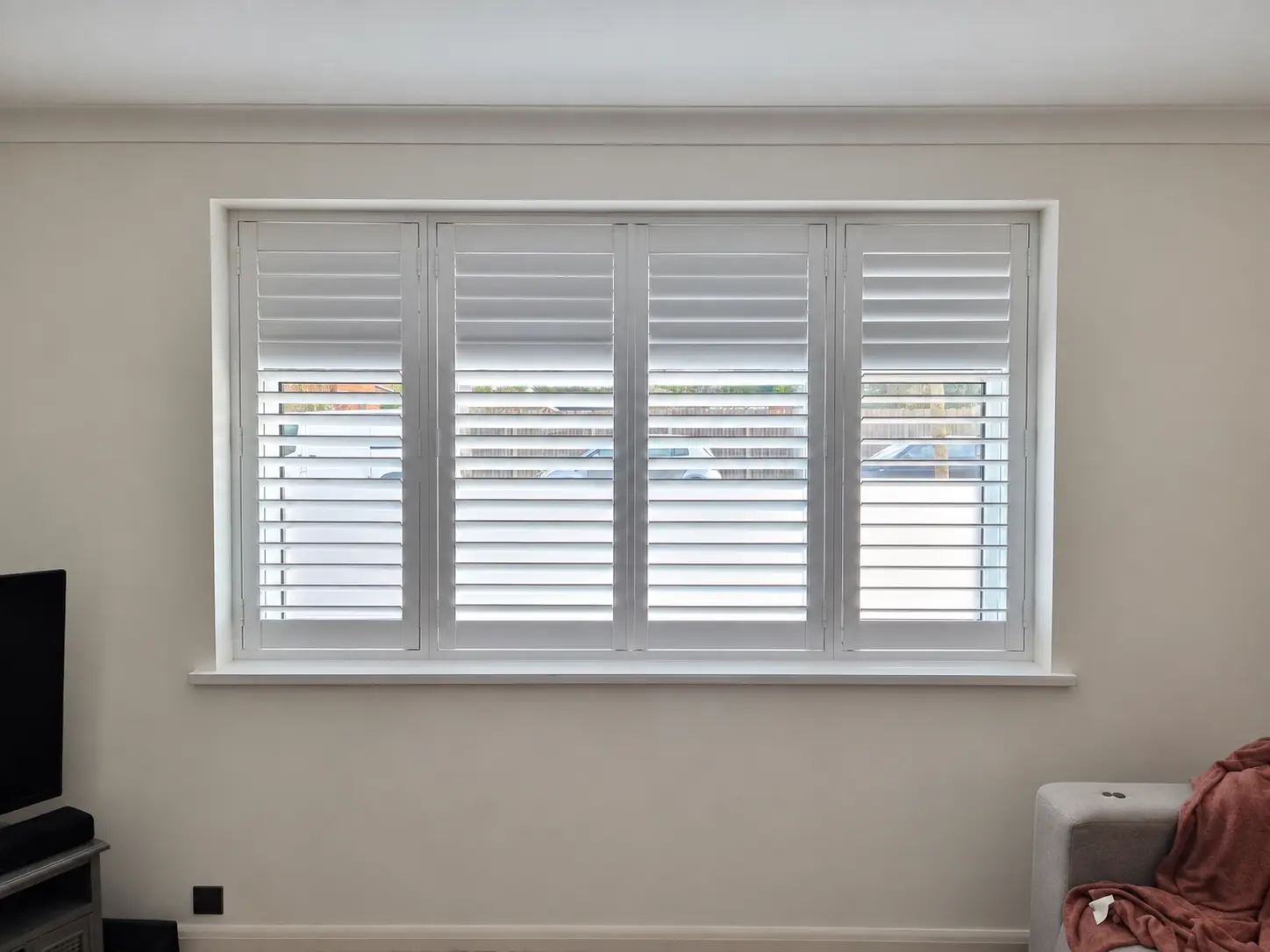 Four white full-height shutter panels across a living-room window, with upper louvres closed and lower louvres open.
