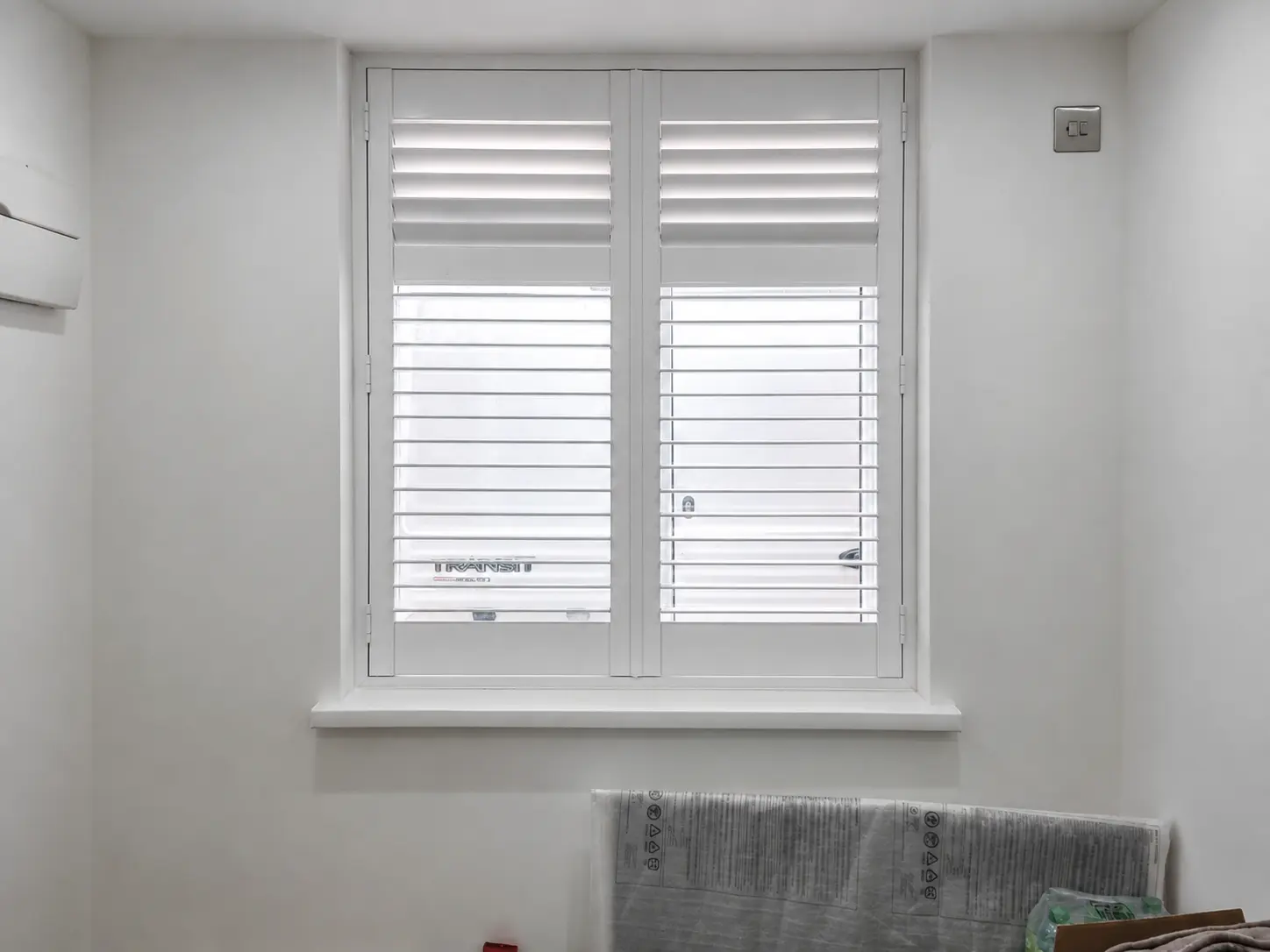 Two white full-height shutter panels at an office window, with upper louvres closed and lower louvres open.