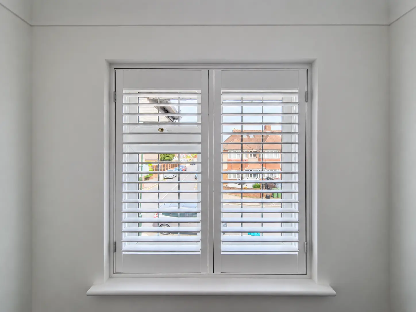 Two white full-height shutter panels at an office window, with the louvres open.