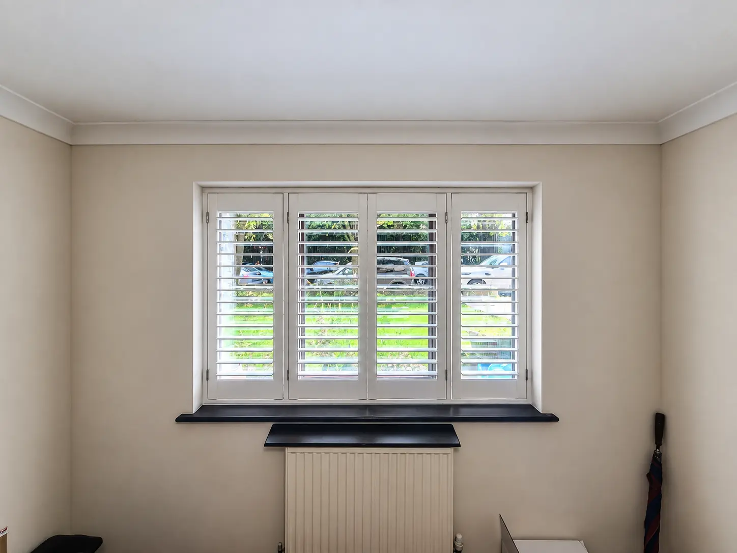 Four white full-height shutter panels at an office window above a dark sill and radiator.