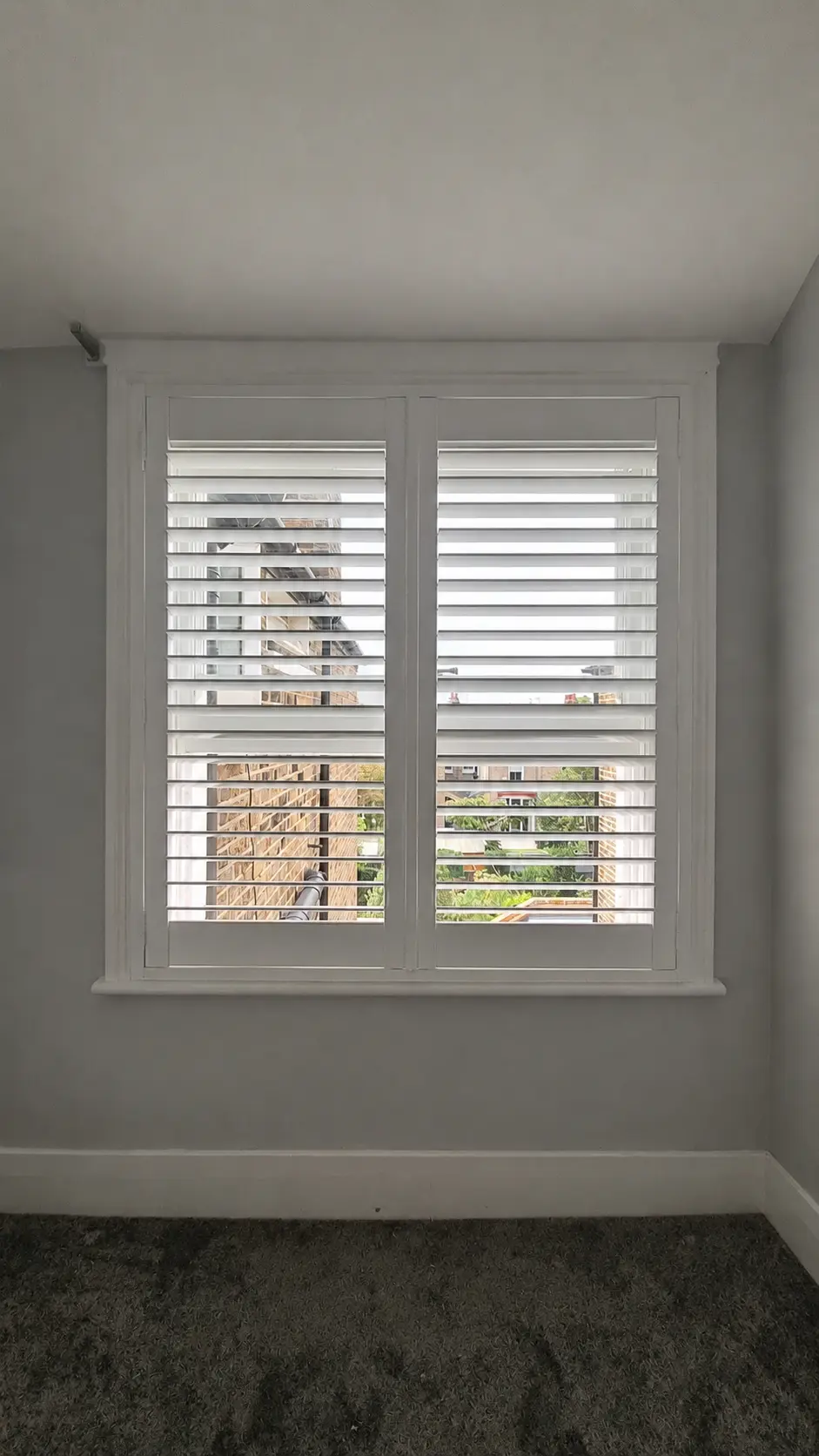 Two white full-height shutter panels at an office window in a narrow grey-painted recess.
